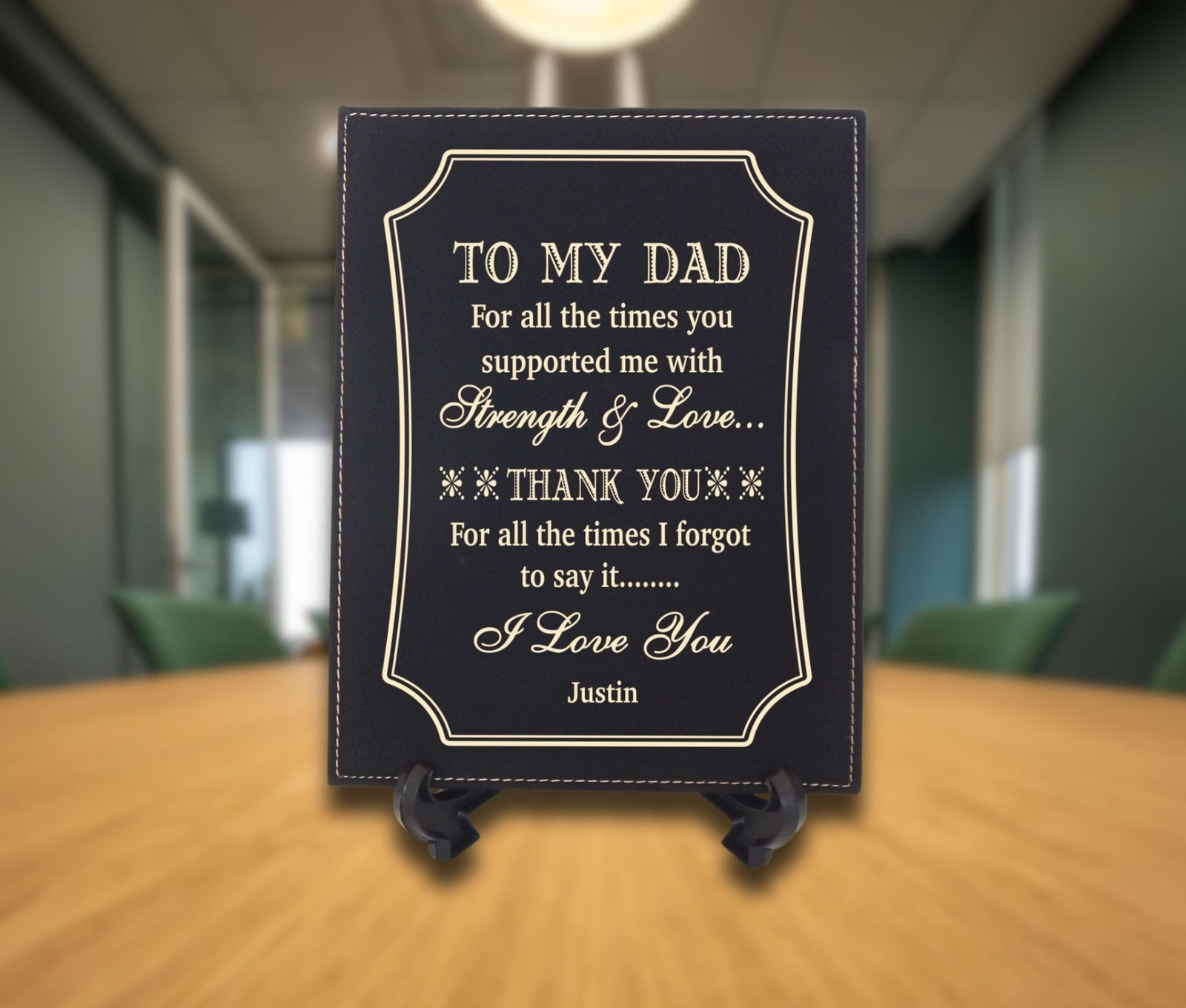 A personalized black plaque with gold lettering that reads 'TO MY DAD' and a thank you message, displayed on a small black stand on a wooden table with a blurred office background.