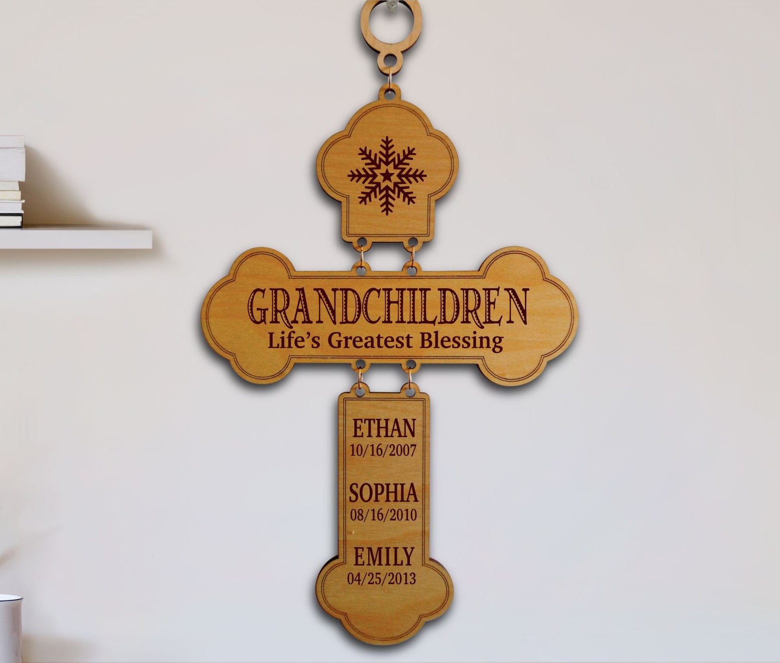 Personalized wooden cross wall plaque engraved with 'GRANDCHILDREN Life's Greatest Blessing' and three hanging nameplates with birth dates and names, shown hanging on a light wall.