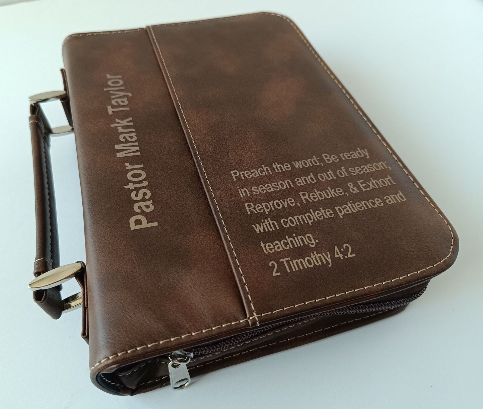 A brown faux-leather Bible cover with a zipper closure and handle, featuring personalized text 'Pastor Mark Taylor' and a scripture quote from 2 Timothy 4:2 on a white background.