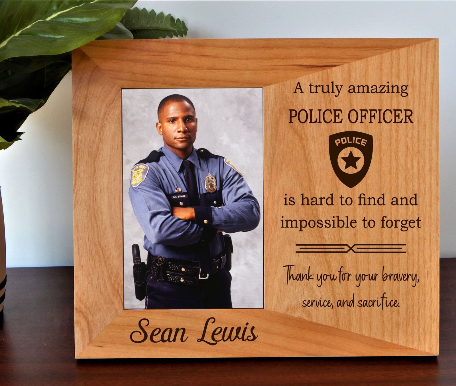 A personalized wooden photo frame plaque engraved with a tribute message for a police officer. The light brown wood frame features a photo slot showing a male police officer in uniform, alongside engraved text reading 'A truly amazing POLICE OFFICER is hard to find and impossible to forget' and 'Thank you for your bravery, service, and sacrifice.