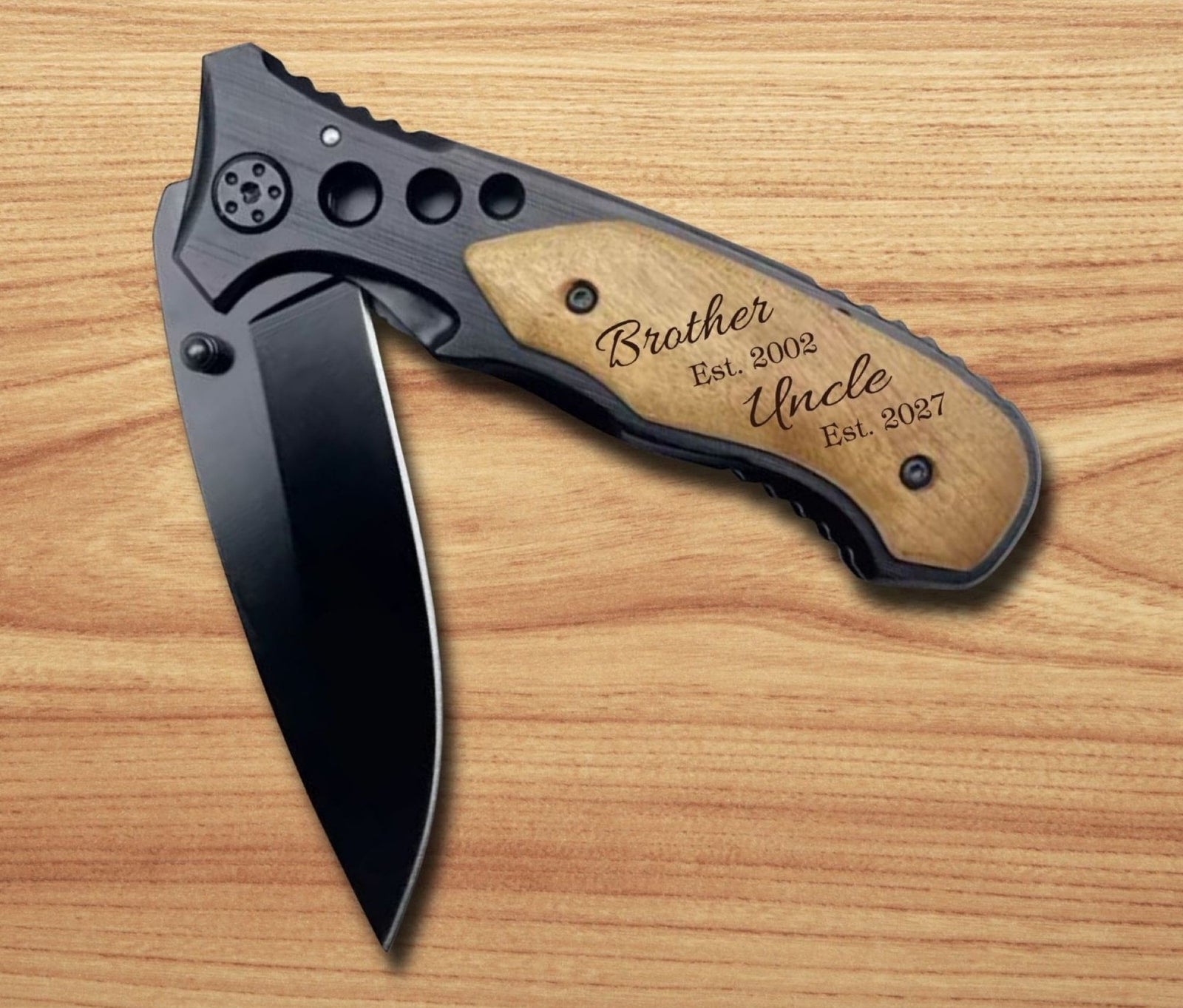 A folding pocket knife with a black blade and black handle, featuring a light wood inlay engraved with 'Brother Est. 2002 Uncle Est.