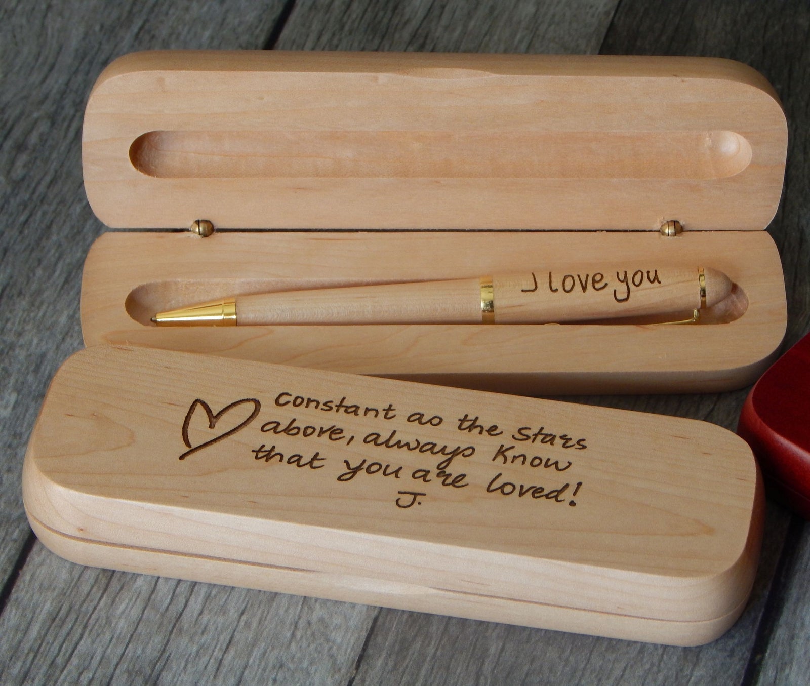 A personalized wooden keepsake box set, featuring an open box with a gold-accented pen inside engraved with 'I love you', and a closed box below engraved with 'Constant as the Stars above, always know that you are loved!' on a gray wood-textured background.