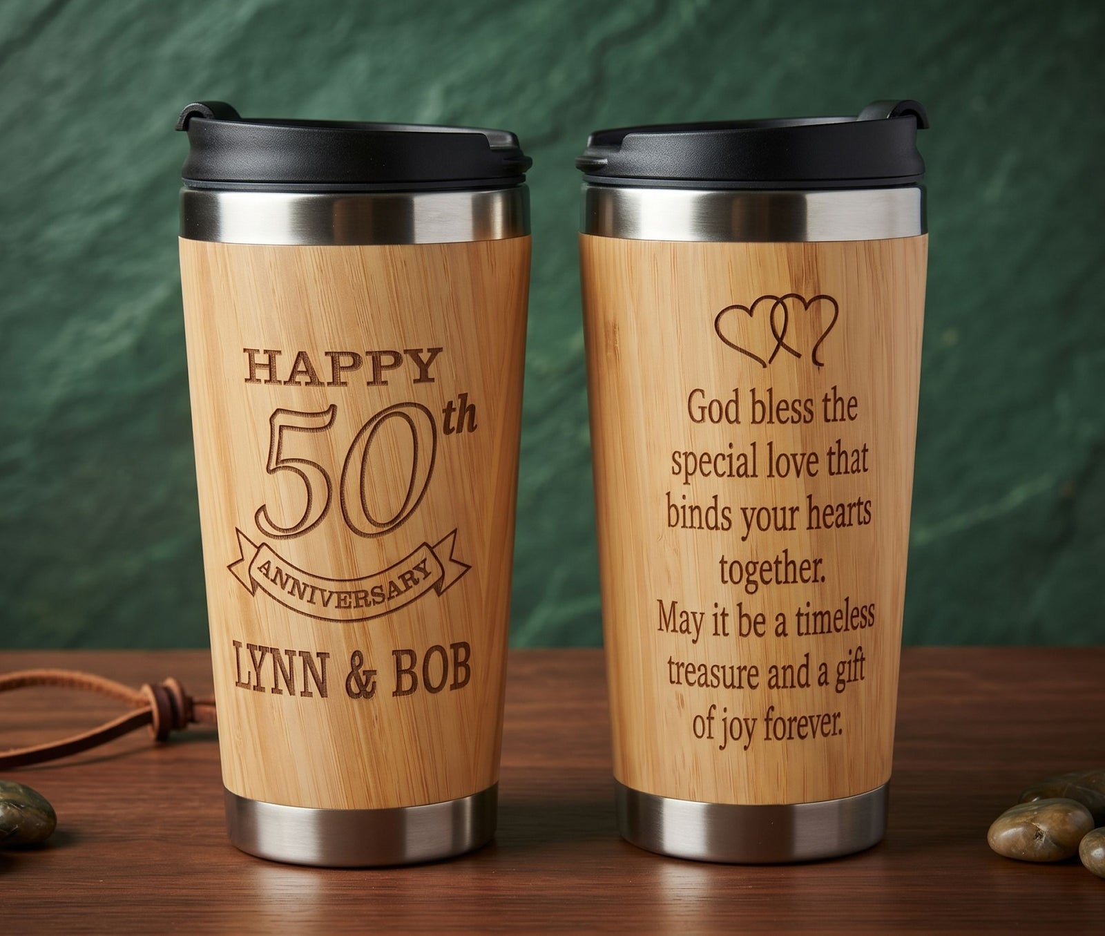 Two personalized wooden travel tumbler cups with black lids, displayed side by side on a wooden surface against a dark green textured background. The left cup is engraved with 'HAPPY 50th ANNIVERSARY LYNN & BOB', and the right cup is engraved with a romantic message starting with 'God bless the special love that binds your hearts together.