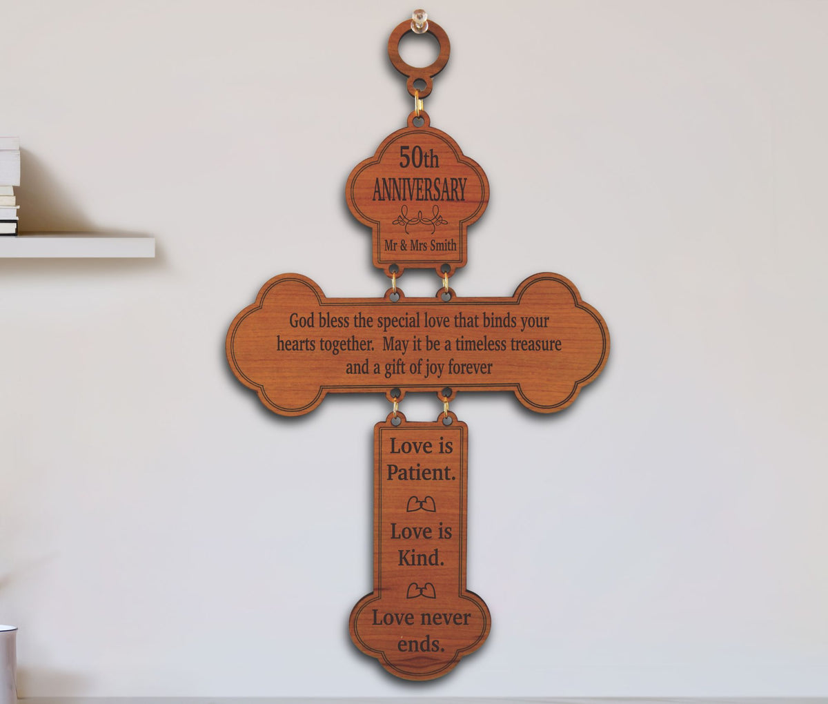 A wooden cross-shaped wall hanging with engraved anniversary and love messages, shown hanging on a white wall.