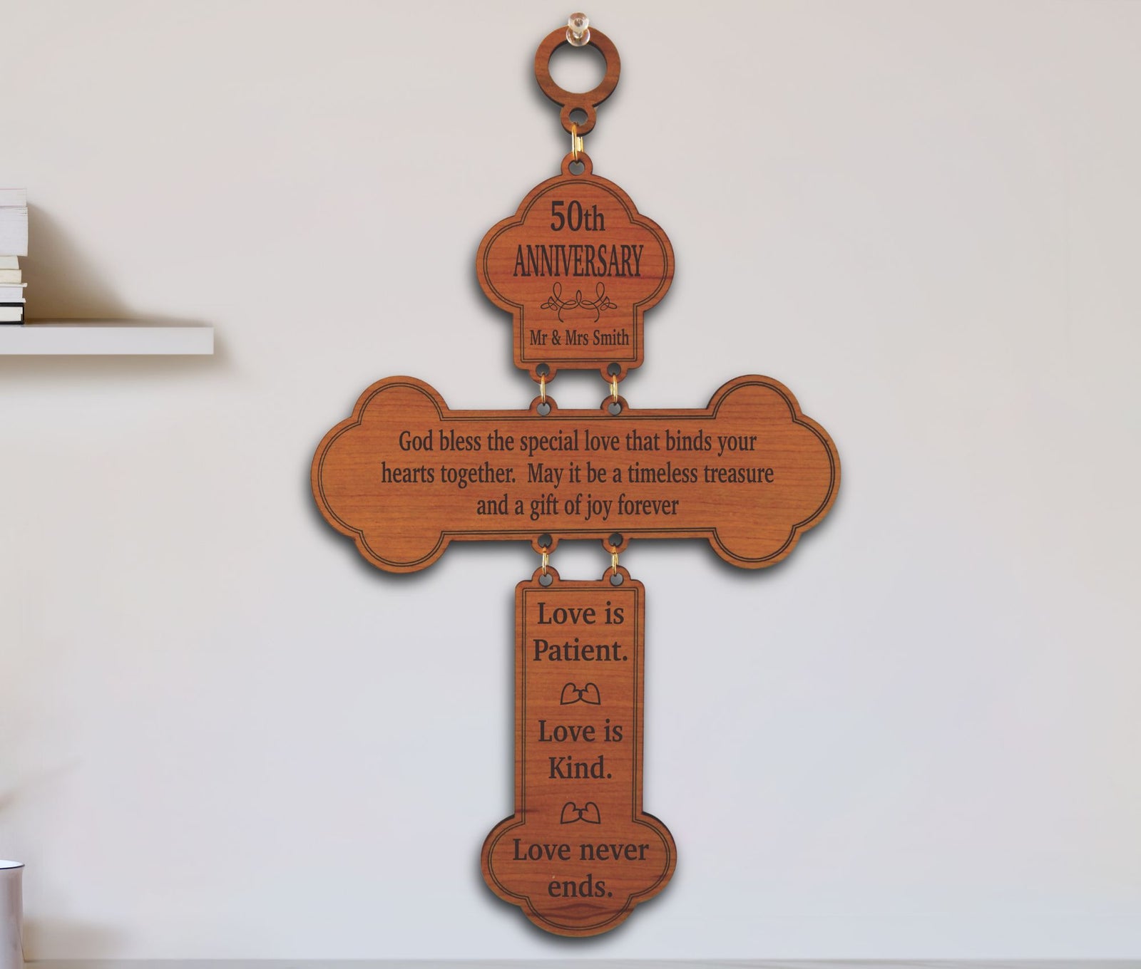 A wooden cross-shaped wall hanging with engraved anniversary and love messages, shown hanging on a white wall.