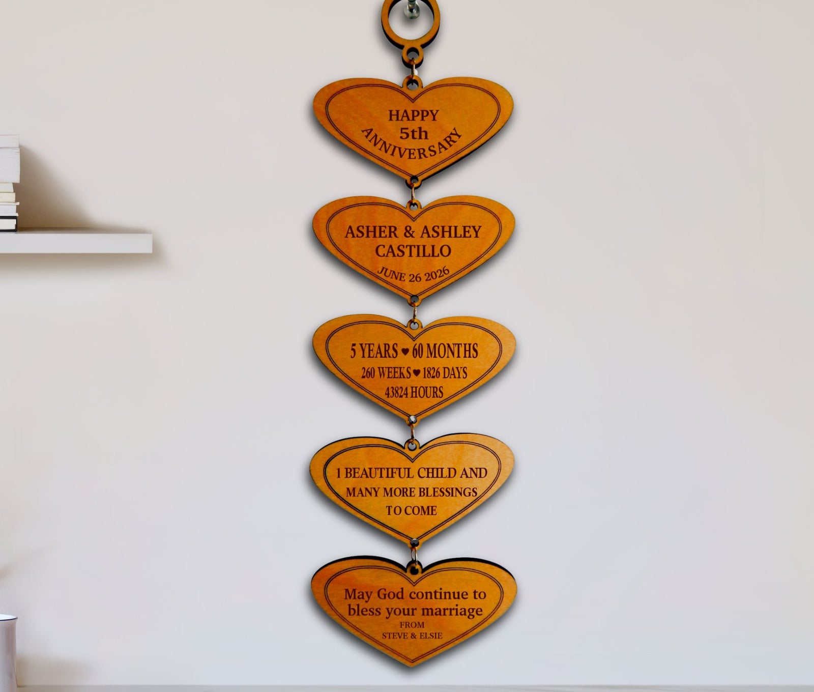 A vertical wooden anniversary wall hanging made of five connected heart-shaped plaques with engraved milestone messages, mounted on a white wall.
