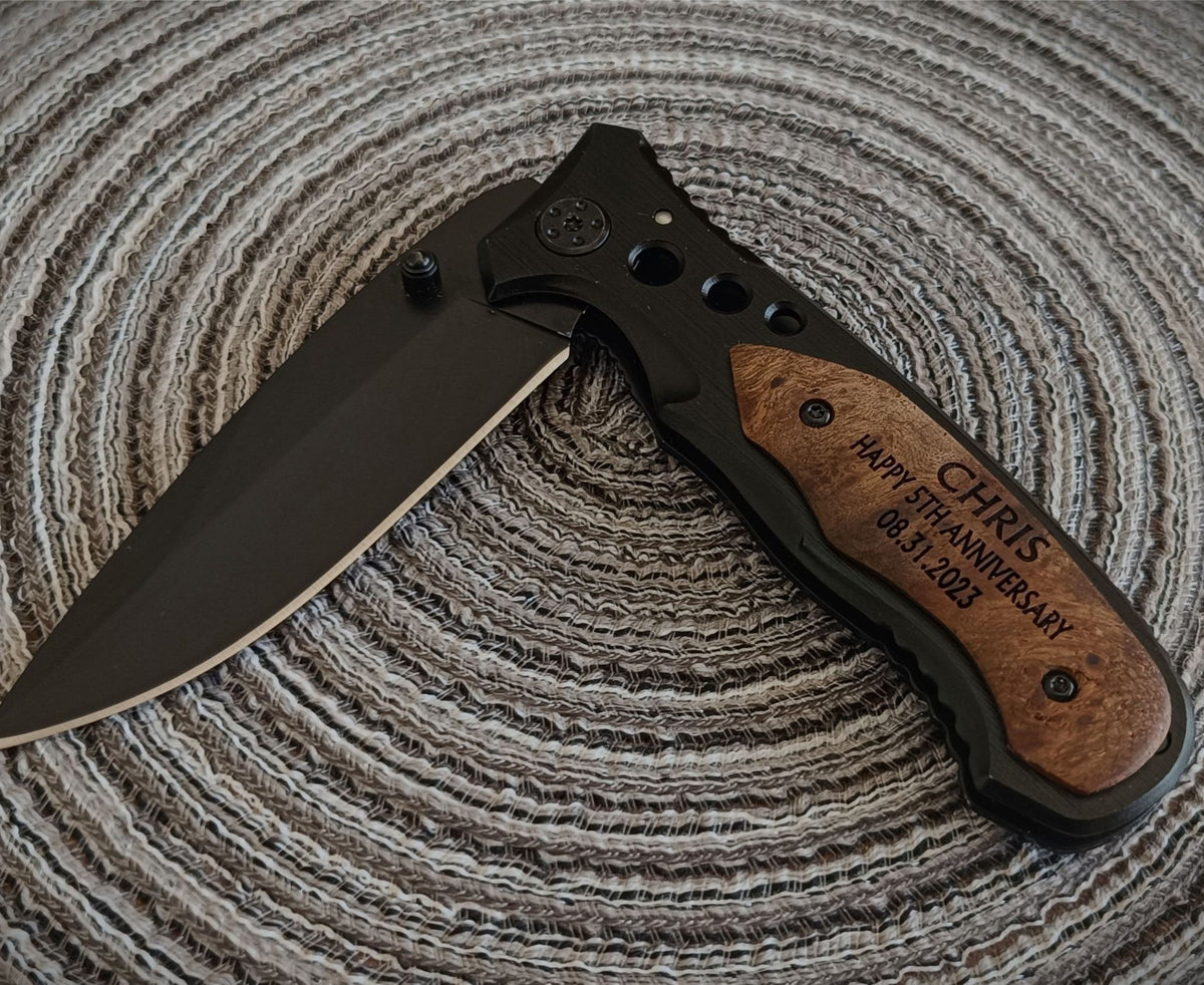 A custom folding pocket knife with a matte black blade and a brown wood-grain handle scale engraved with 'CHRIS HAPPY 35th ANNIVERSARY 08.31.