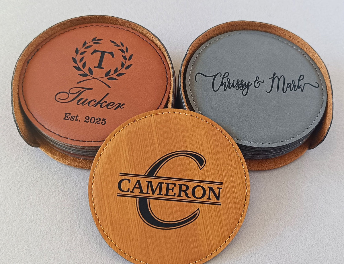 Three round personalized leather coasters displayed on a light neutral background. One coaster in the front is light tan wood with a black monogram 'C' and the name 'CAMERON'.