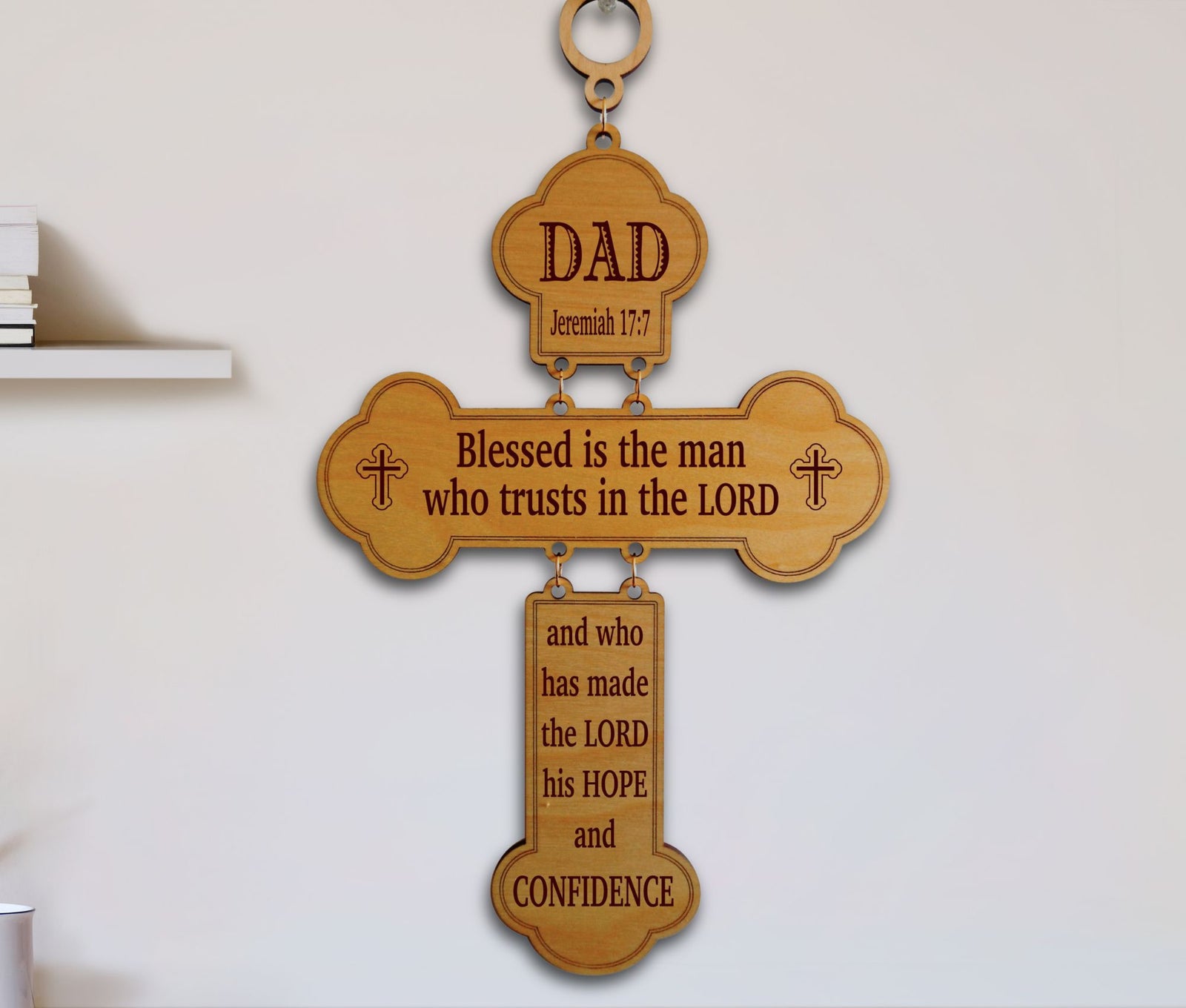 A wooden cross wall hanging with engraved religious text, including 'DAD' at the top and a Bible verse from Jeremiah 17:7, displayed against a plain light wall.