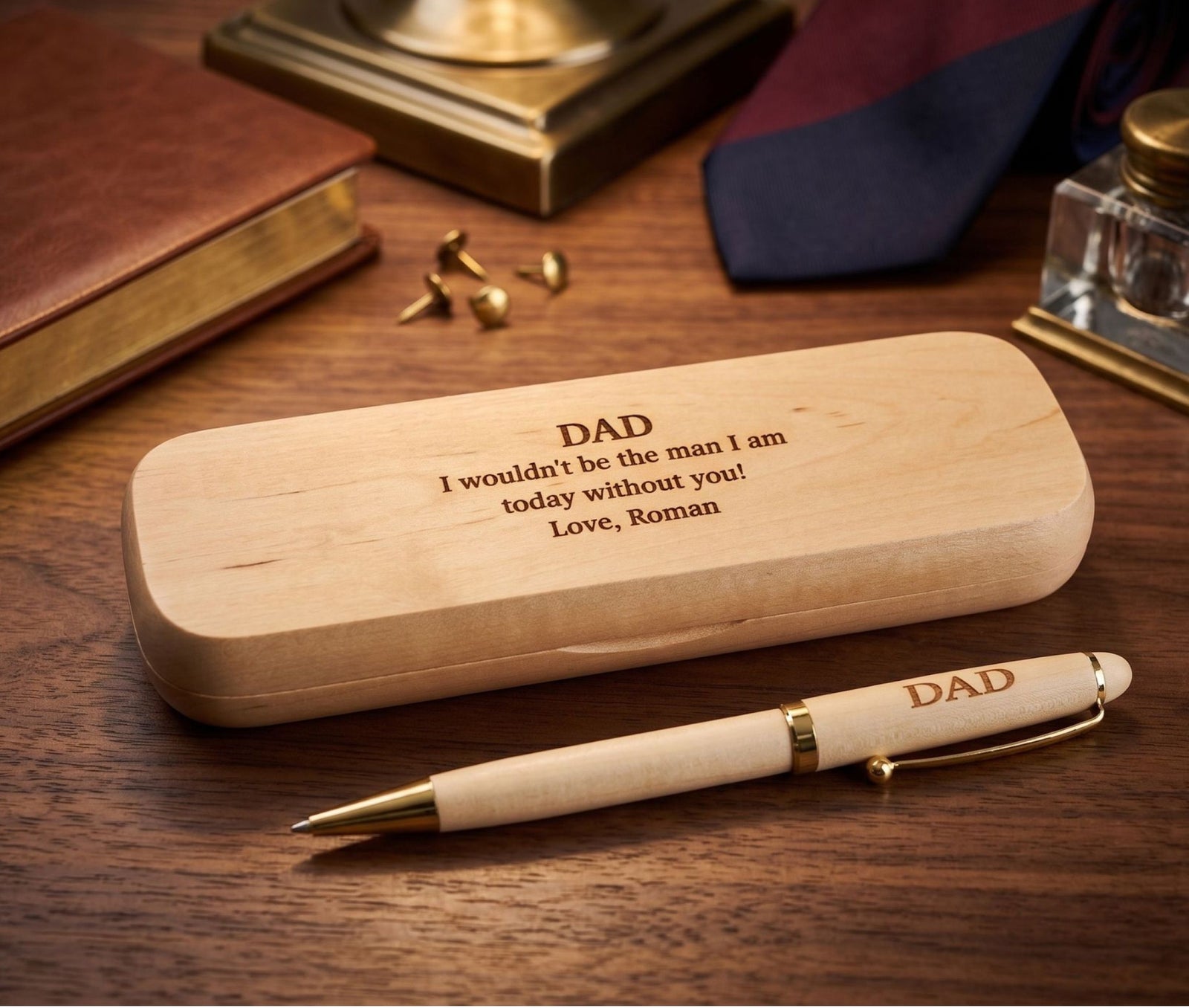 Personalized wooden pen and matching wooden case engraved with 'DAD I wouldn't be the man I am today without you! Love, Roman' on a wooden desk with a tie, cufflinks, and other desk accessories in the background.