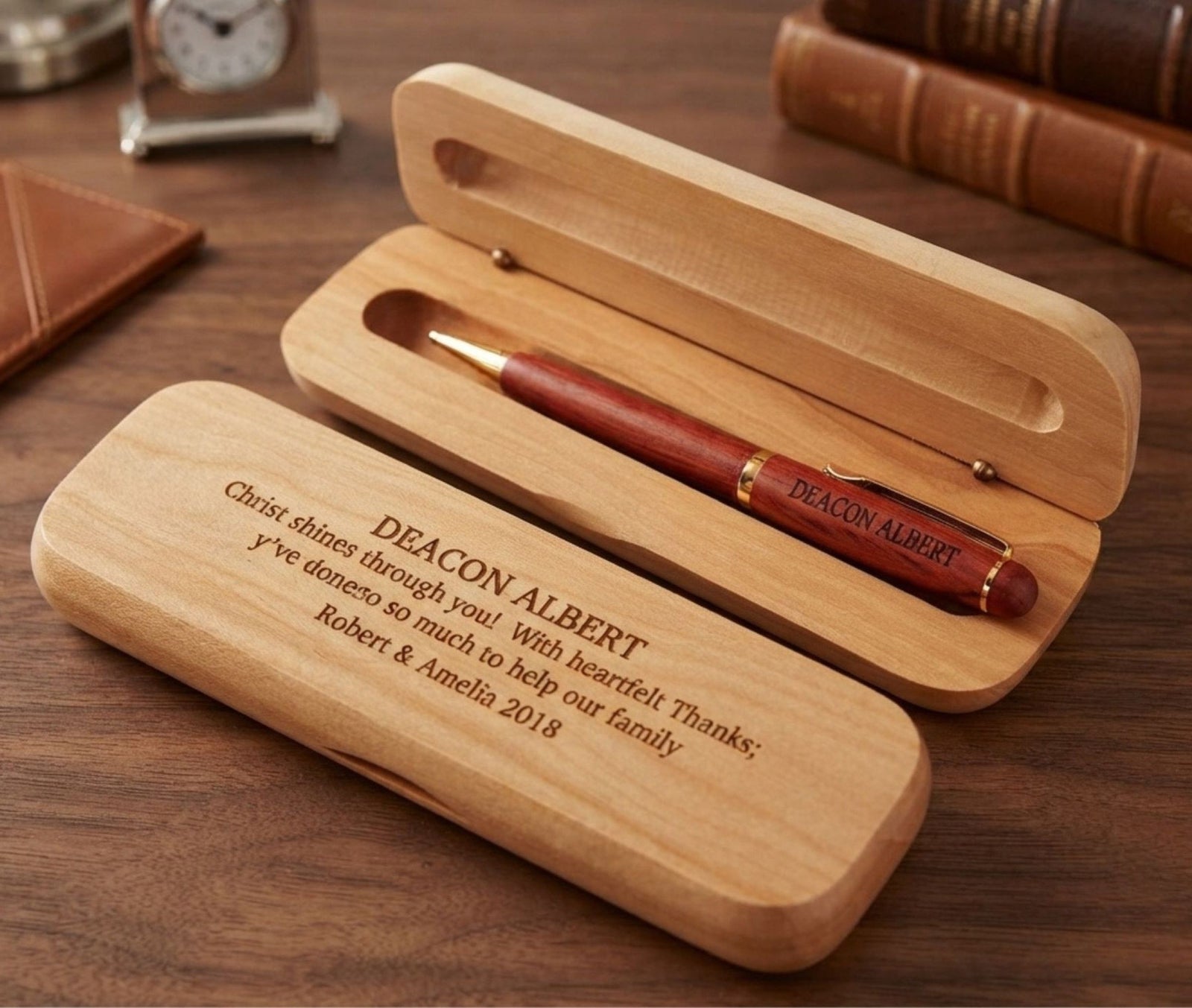 Personalized wooden pen case set with an engraved wooden box and a red-brown pen with gold trim, displayed on a wooden desk with books in the background.
