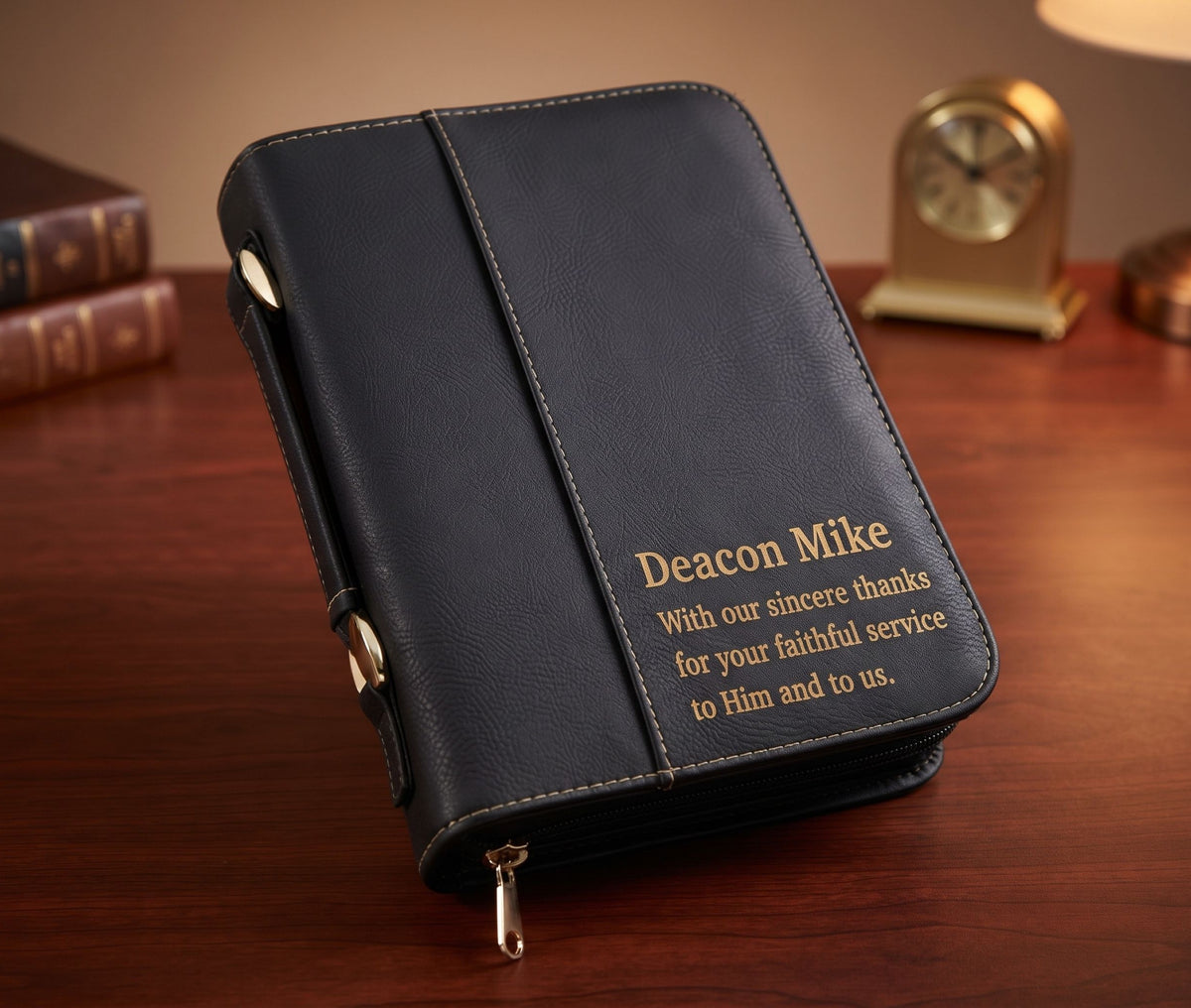 A black leather-bound journal or Bible cover with gold text reading 'Deacon Mike' and a thank-you message, placed on a wooden desk with a blurred clock and books in the background.