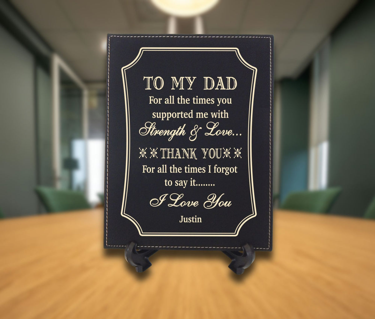 A personalized black plaque with gold lettering that reads 'TO MY DAD' and a thank you message, displayed on a small black stand on a wooden table with a blurred office background.