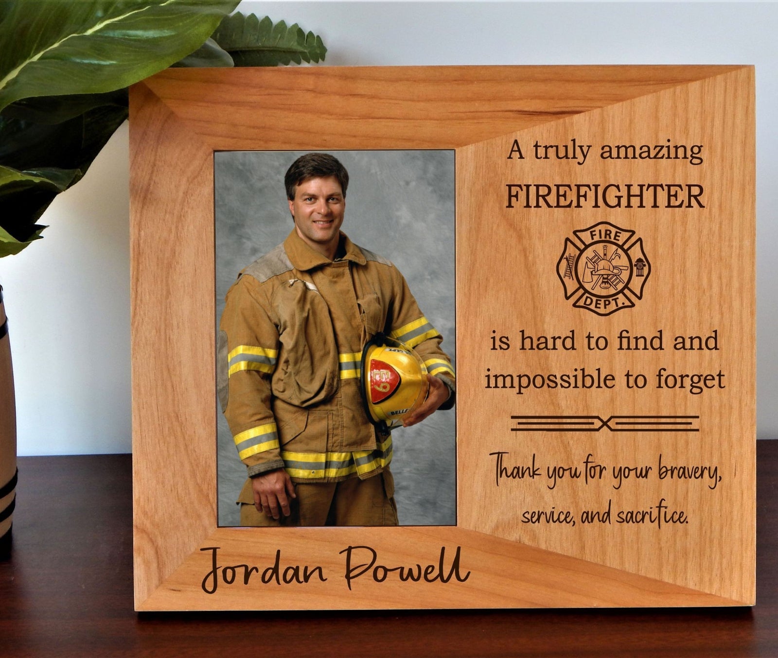 Personalized wooden firefighter memorial plaque engraved with 'Jordan Powell' and a photo of a firefighter holding a helmet, displayed on a tabletop with a plant leaf in the background.