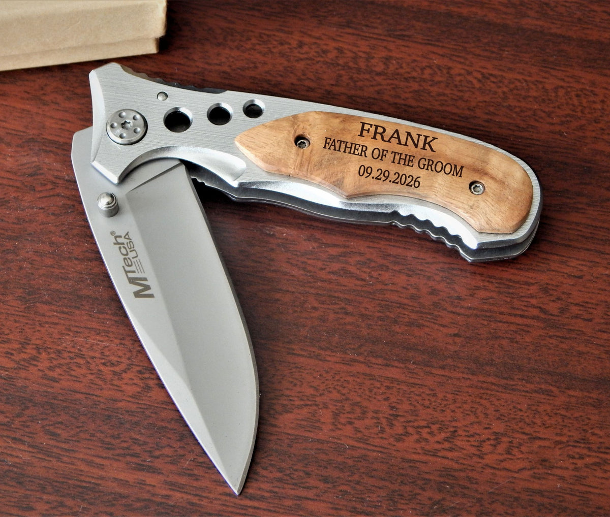 A custom folding pocket knife with a silver stainless steel blade and handle, featuring a light wood inlay engraved with 'FRANK FATHER OF THE GROOM 09.29.