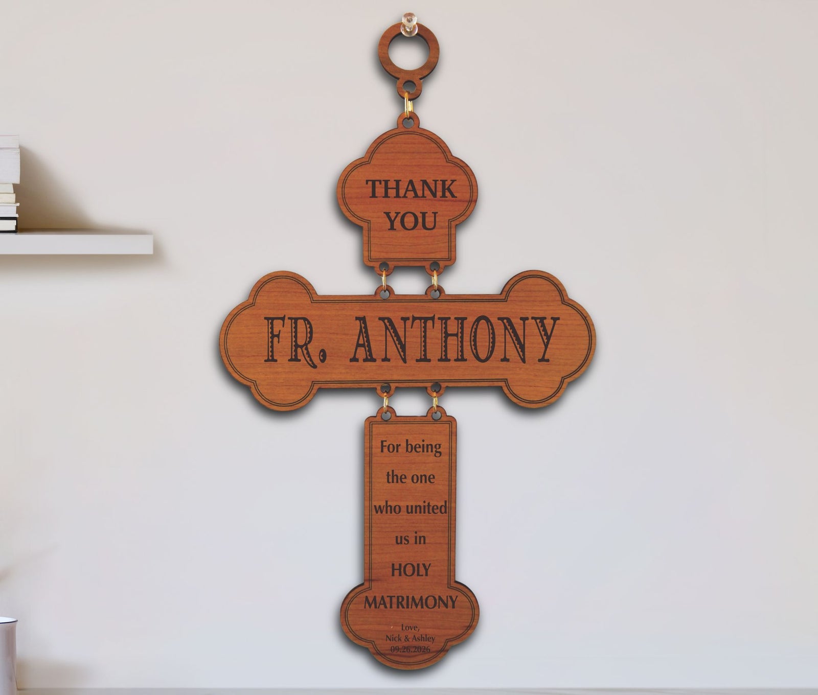A wooden hanging cross plaque with engraved text reading 'THANK YOU', 'FR. ANTHONY', and 'For being the one who united us in HOLY MATRIMONY', displayed against a white wall.