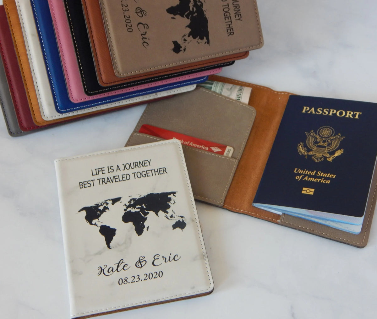 Two engraved leather passport holders, one with a world map and the other with text, alongside a set of documents such as a passport and a visa.