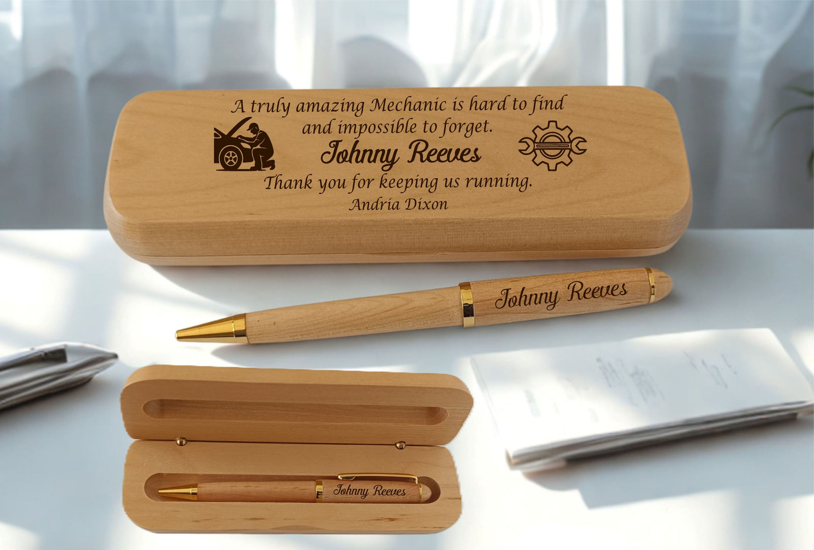 Personalized wooden pen and matching wooden case set on a white desk with a blurred office background. The engraved text reads 'A truly amazing Mechanic is hard to find and impossible to forget, Thank you for keeping us running,  with small engraved illustrations.