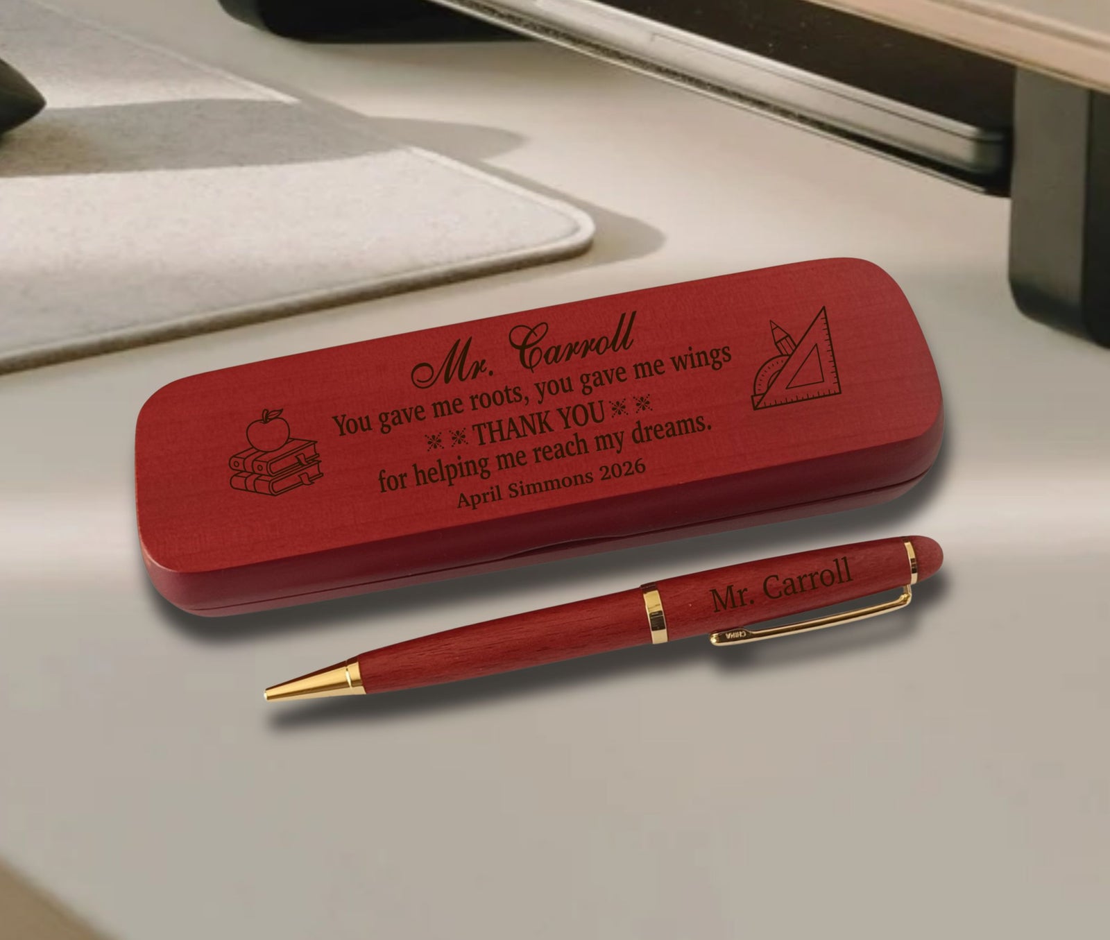 A personalized red wooden pen and matching pencil case set engraved with the name 'Mr. Carroll' and a thank-you message, displayed on a light gray desk.