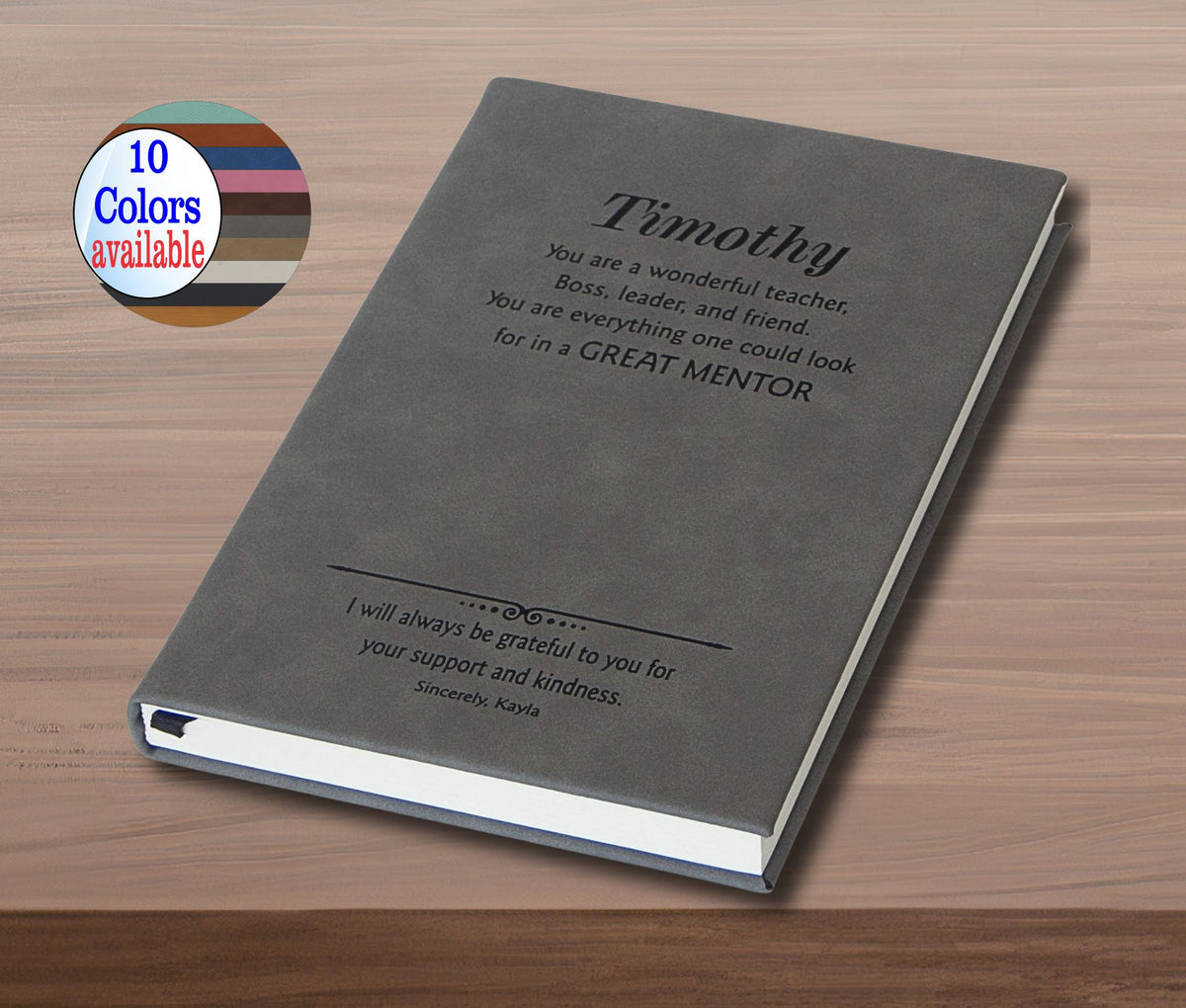 A personalized hardcover notebook or journal shown at an angle on a wooden surface. The cover is dark gray with black printed text reading 'Timothy' and a mentor message.