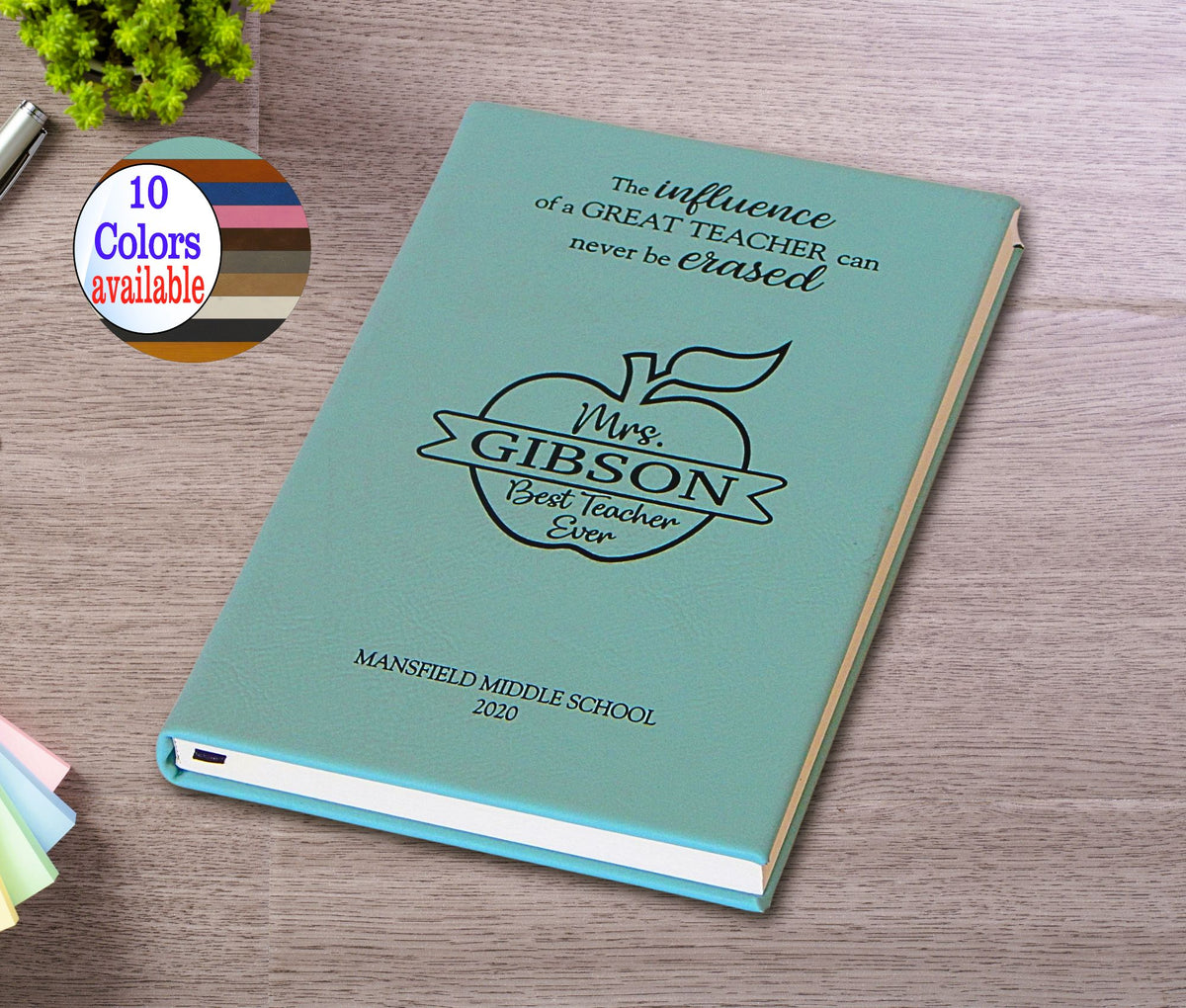A personalized hardcover teacher appreciation book or notebook in a light teal color, featuring a black printed apple logo and the text 'Mrs. Gibson Best Teacher Ever' and 'Mansfield Middle School 2020'.