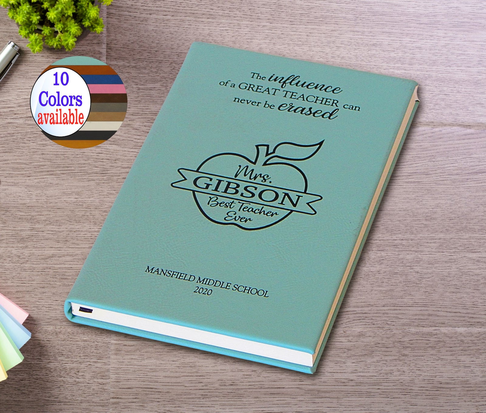 A personalized hardcover teacher appreciation book or notebook in a light teal color, featuring a black printed apple logo and the text 'Mrs. Gibson Best Teacher Ever' and 'Mansfield Middle School 2020'.