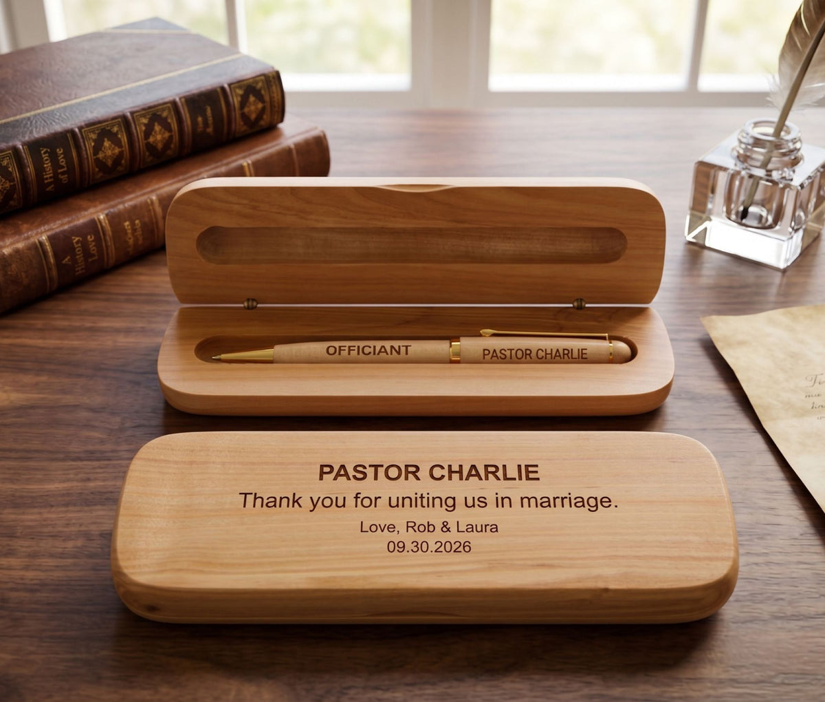 Personalized wooden wedding keepsake box set on a wooden desk, featuring an open box with a gold pen inside and a closed lid engraved with 'PASTOR CHARLIE Thank you for uniting us in marriage. Love, Rob &amp; Laura 09.