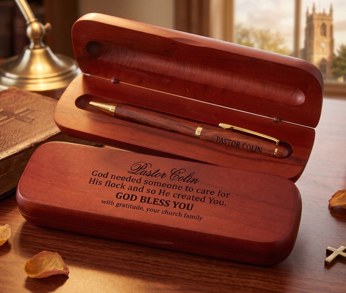 A personalized wooden keepsake box set on a wooden desk, featuring an open box with a matching wooden pen inside and a closed box in front with engraved text. The scene is styled with a book, succulents, and papers on a warm wooden table.