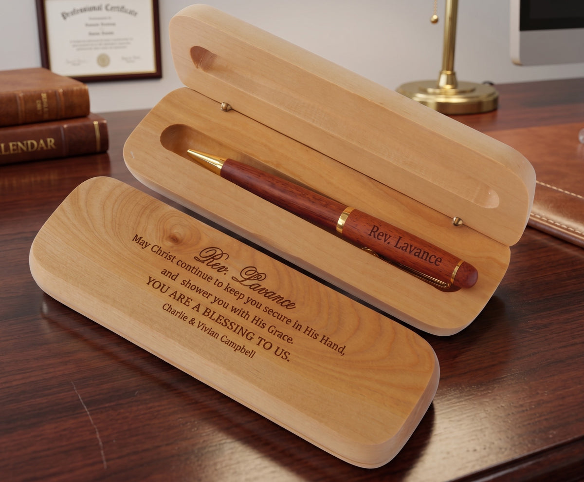 A personalized wooden pen presented in an open matching wooden case on a dark wood desk, with a lamp and framed certificate visible in the background.