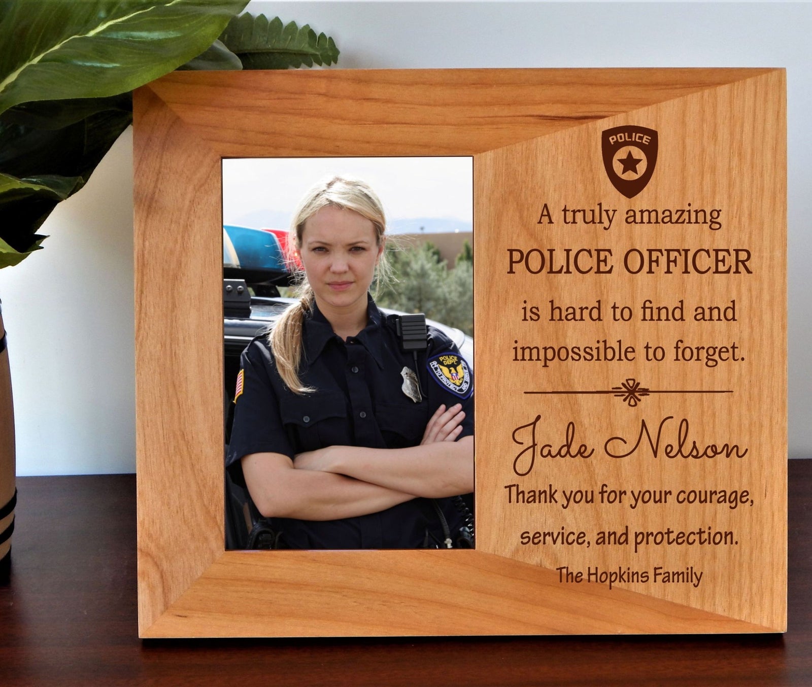 A personalized wooden photo frame with engraved text honoring a police officer. The frame has a natural light brown wood finish, a custom photo slot showing a female officer, and engraved text that reads 'A truly amazing POLICE OFFICER is hard to find and impossible to forget.