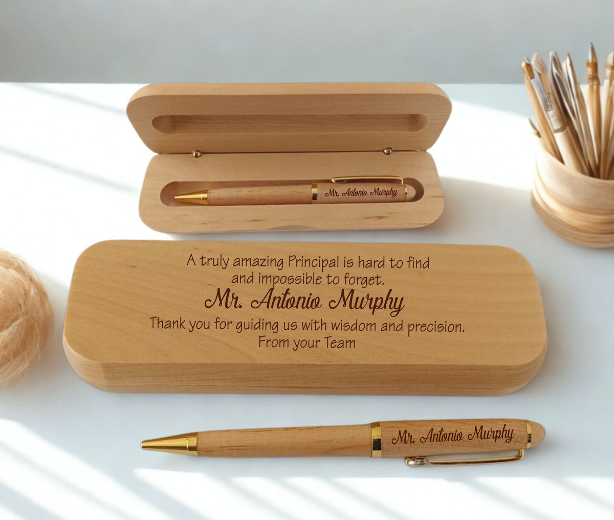 A personalized wooden pen and matching wooden case set on a white surface with soft natural shadows. The engraved text reads, 'A truly amazing Principal is hard to find and impossible to forget, Mr.