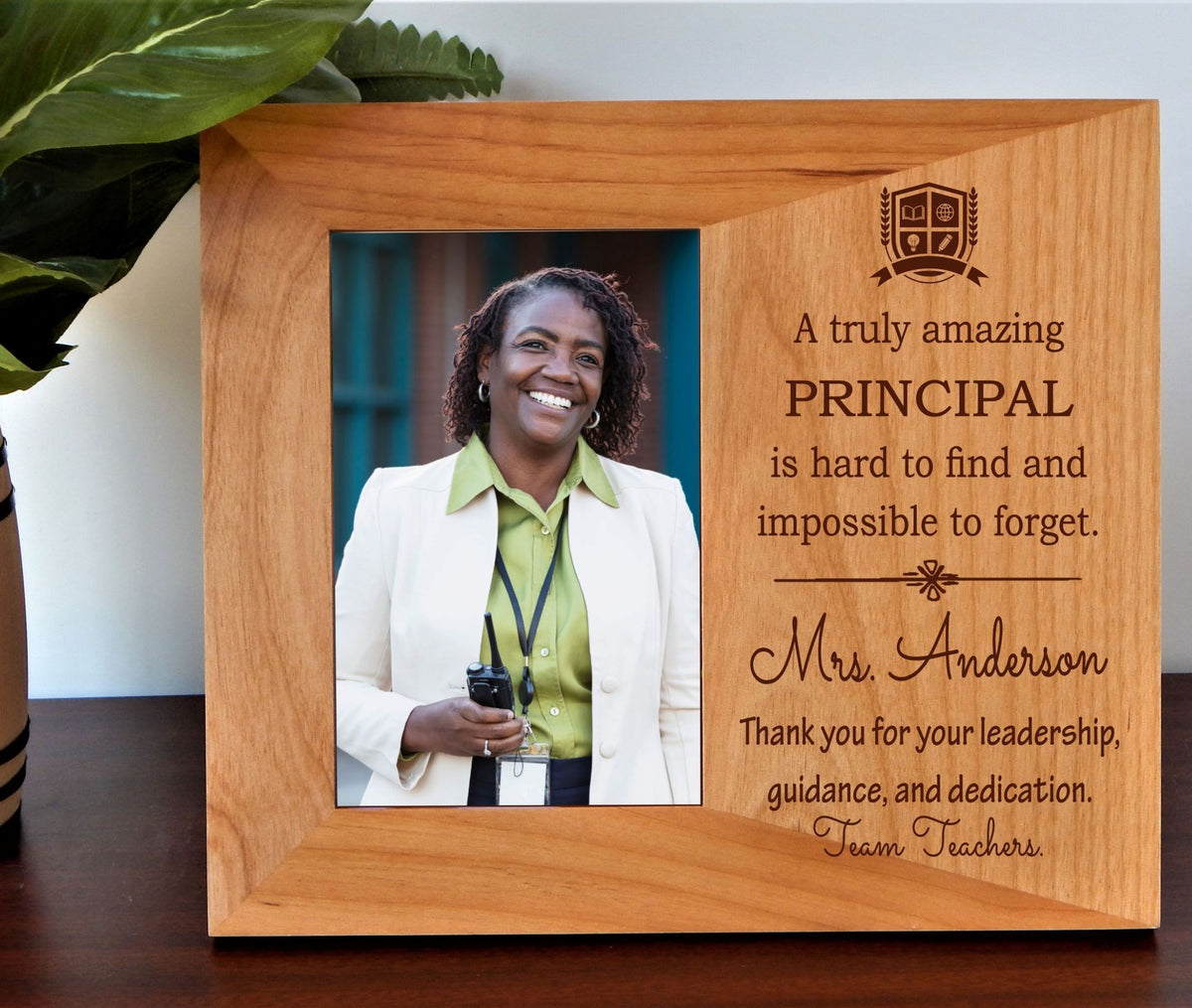 A personalized wooden plaque picture frame on a dark wooden table, featuring a photo of a smiling principal and engraved text thanking her.