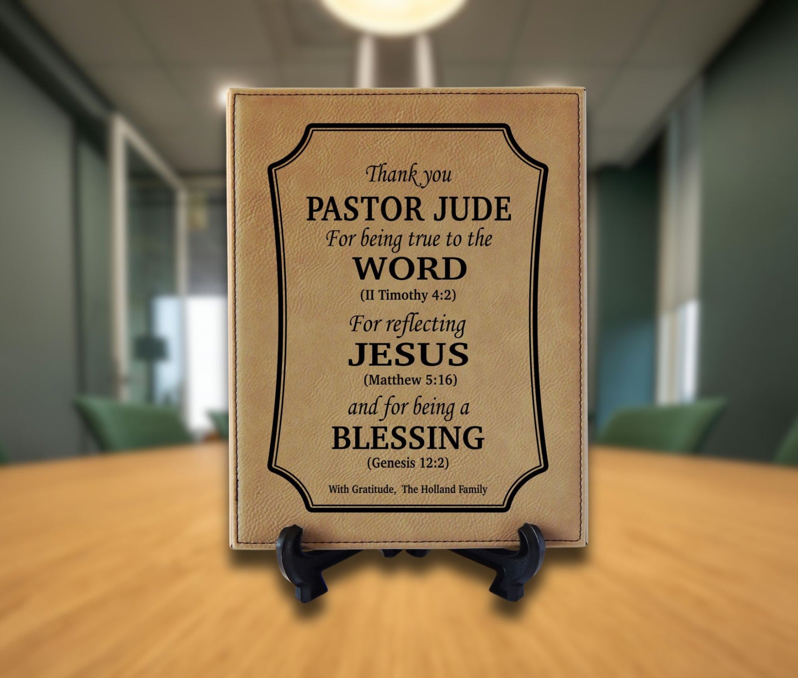 A personalized tan leather plaque with black text on a small black display stand, set against a blurred office background.