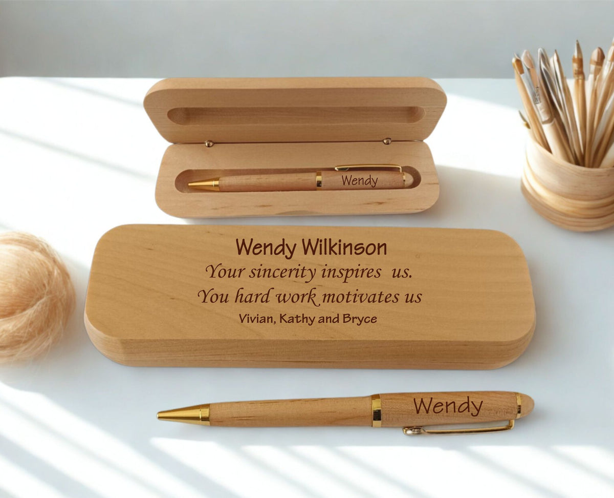 Personalized wooden pen and matching wooden presentation box set on a white surface with soft natural shadows. The engraved text on the front lid reads 'Wendy Wilkinson' with custom messages below, and the pen is engraved with 'Wendy' on the clip.