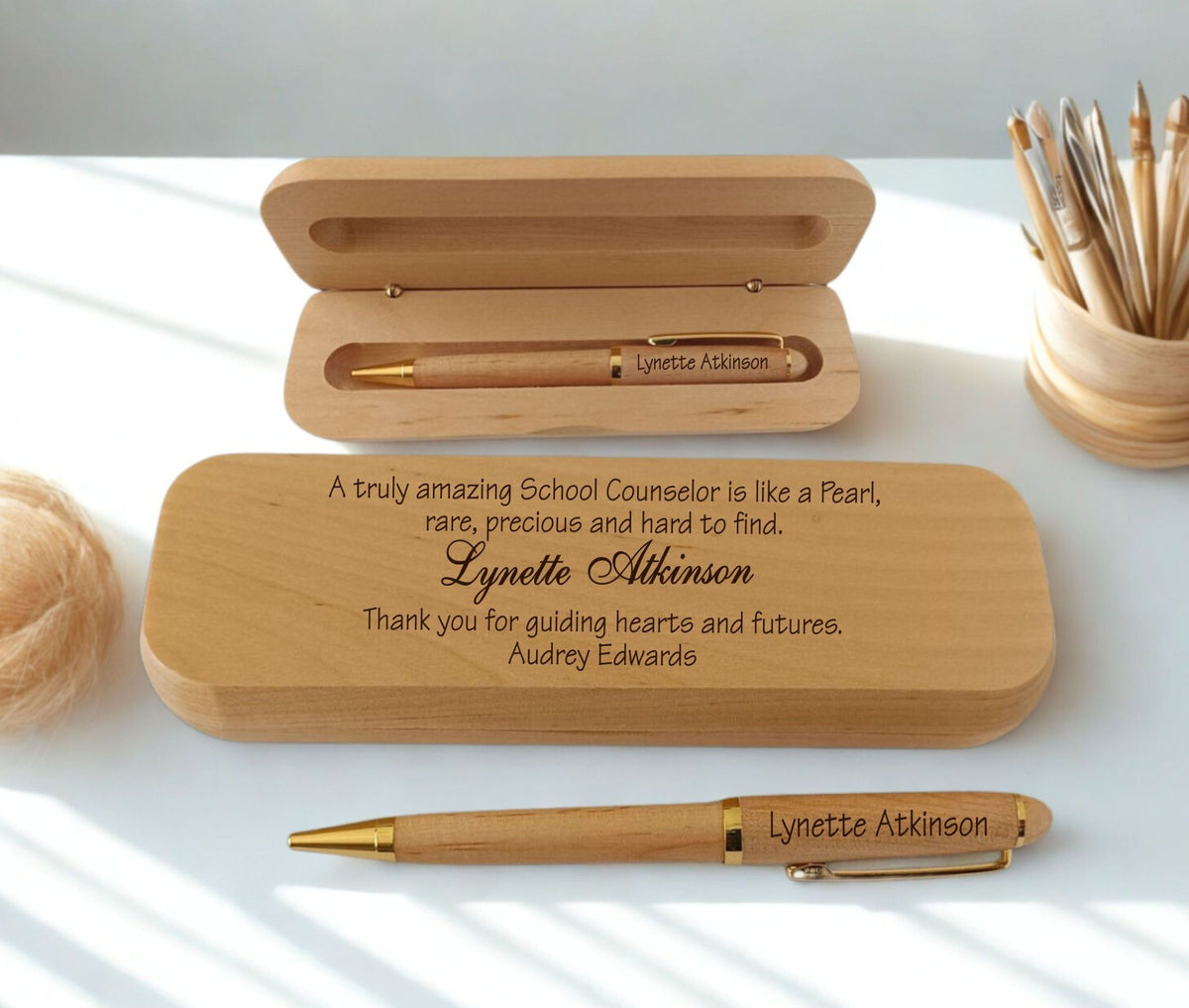 Personalized wooden pen gift set with engraved text, shown with an open wooden case, a closed engraved wooden box, and a gold-accented pen on a white surface with soft natural shadows.
