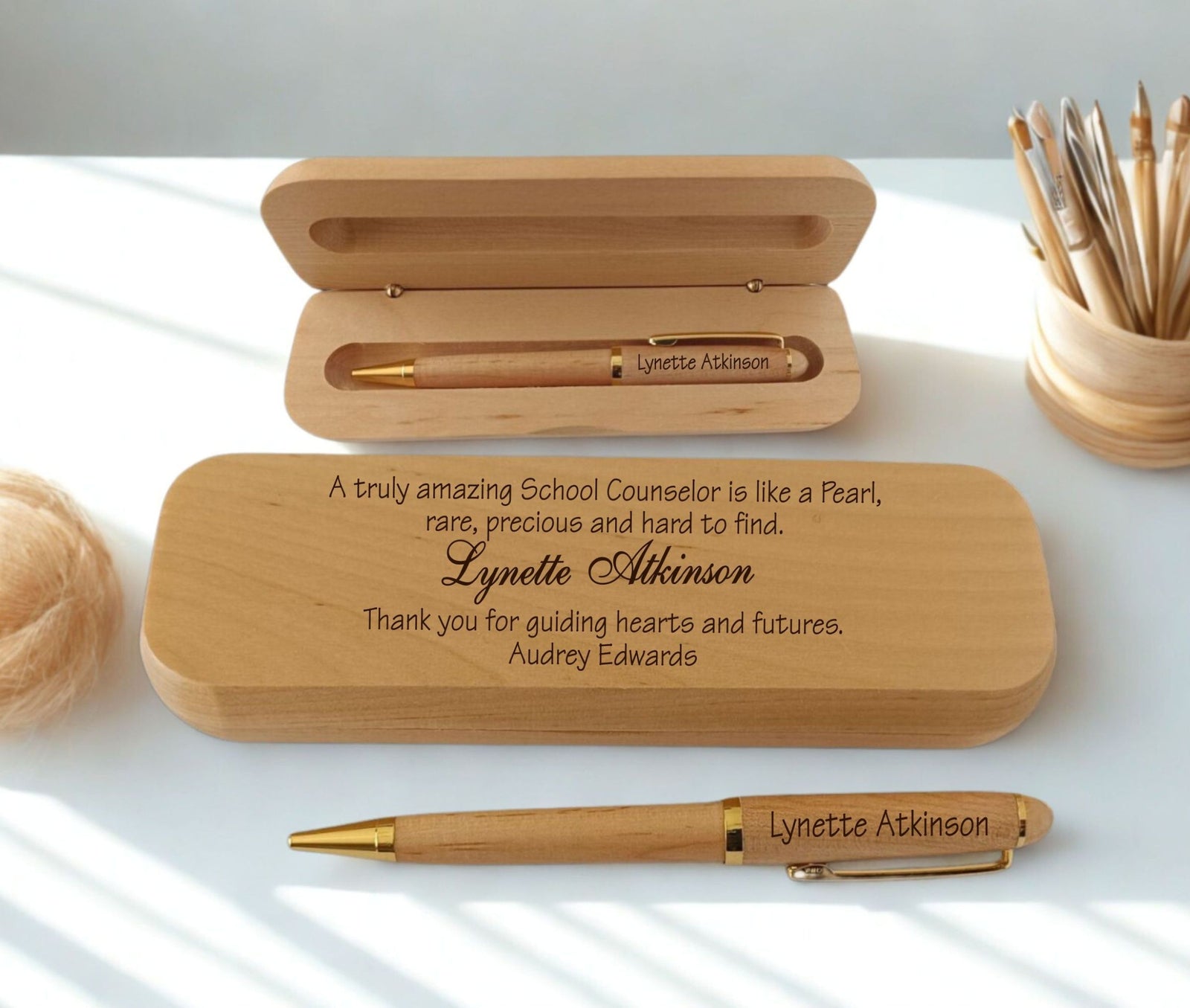 Personalized wooden pen gift set with engraved text, shown with an open wooden case, a closed engraved wooden box, and a gold-accented pen on a white surface with soft natural shadows.