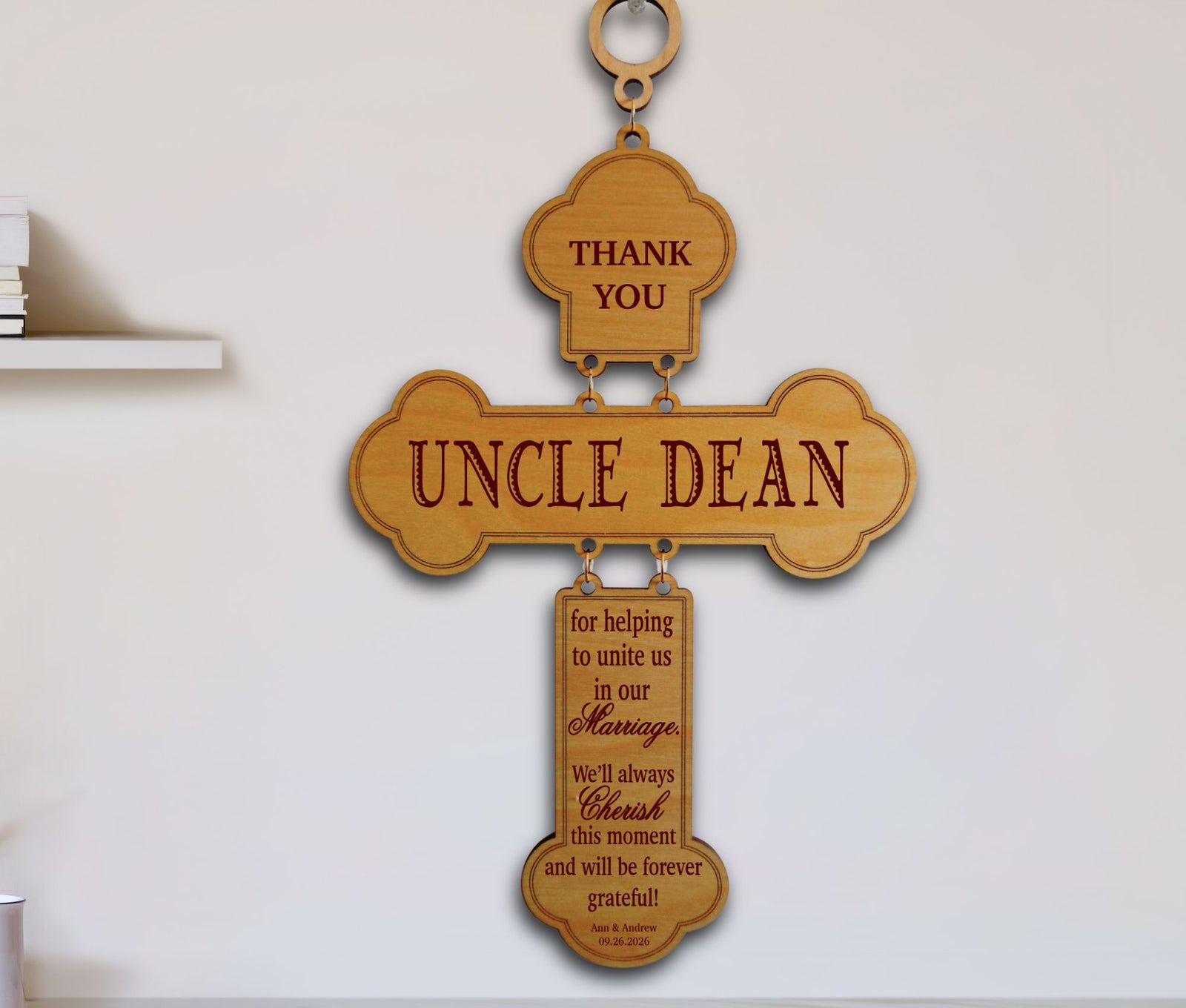 A wooden hanging wall sign shaped like a cross with engraved text reading 'UNCLE DEAN' and additional memorial-style text on a smaller lower pendant, displayed against a light wall.