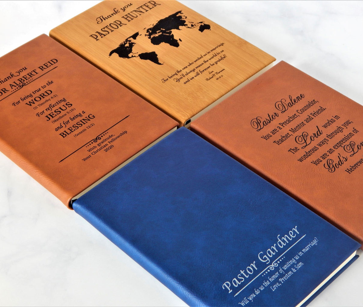 Four personalized leather hardcover  journal notebook arranged on a light marble surface, each with different engraved names and Easter-themed scripture. The covers are in brown, tan, blue, and terracotta orange, with black and white text details.