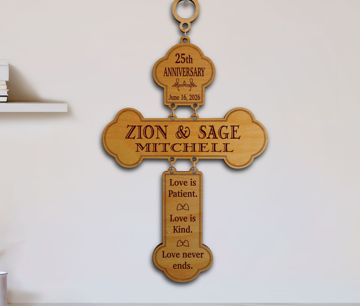 A personalized wooden cross wall plaque engraved with '25th Anniversary' at the top, the names 'ZION &amp; SAGE MITCHELL' in the center, and 'Love is Patient. Love is Kind.