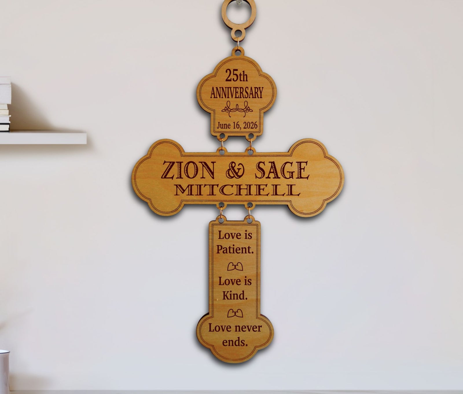A personalized wooden cross wall plaque engraved with '25th Anniversary' at the top, the names 'ZION & SAGE MITCHELL' in the center, and 'Love is Patient. Love is Kind.