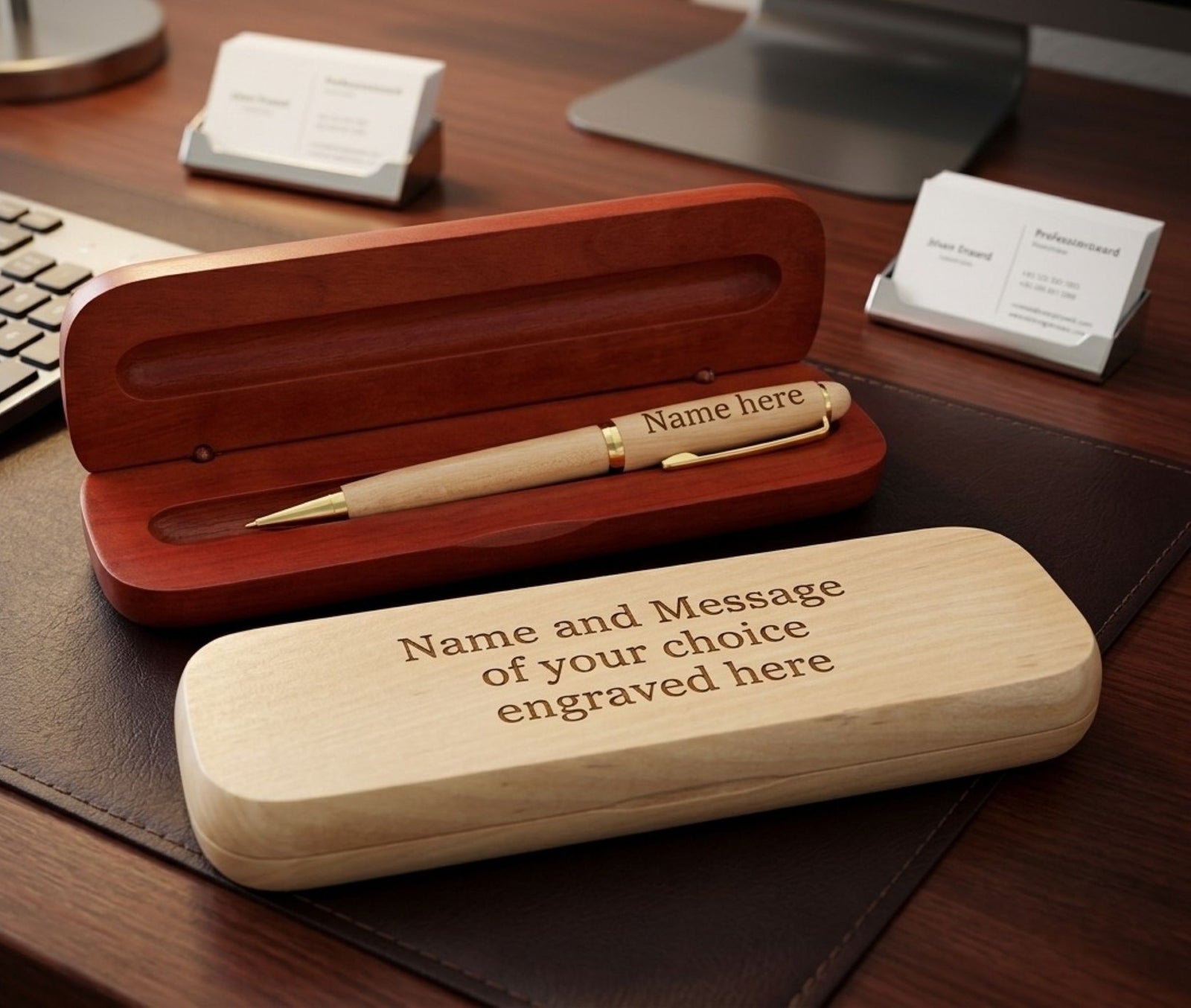 A personalized wooden pen gift set displayed on a dark desk, featuring an open reddish-brown wooden presentation box with a gold-accented pen inside, and a light natural wood engraved case in the foreground.