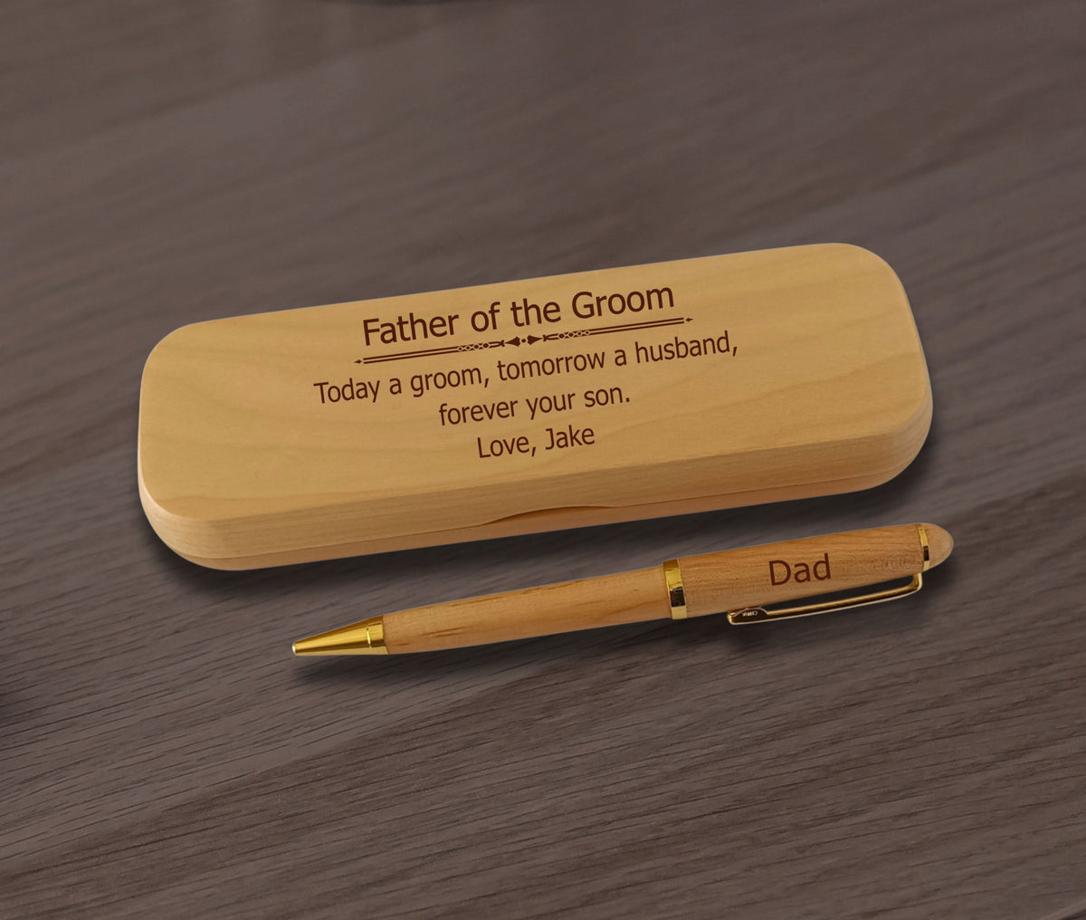 A personalized wooden pen with gold trim and a matching wooden presentation box, both engraved with father-of-the-groom messages, displayed on a dark wood surface.