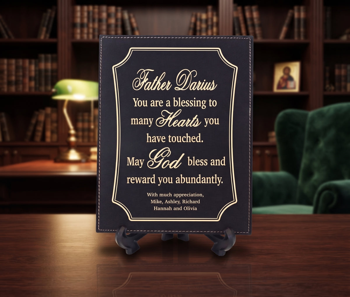 A personalized black plaque with gold lettering on a small black easel stand, placed on a wooden table in front of a blurred library background with a green armchair and lamp.