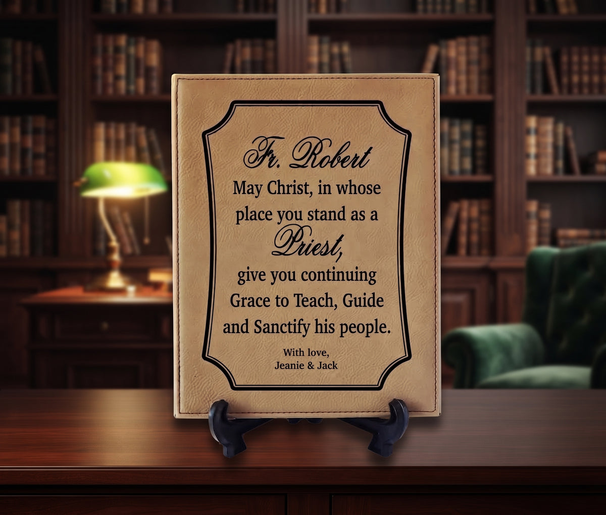 A personalized leather-bound plaque or book cover standing on a small black easel on a wooden desk, with a blurred library interior in the background. The front reads a memorial-style quote for Fr.
