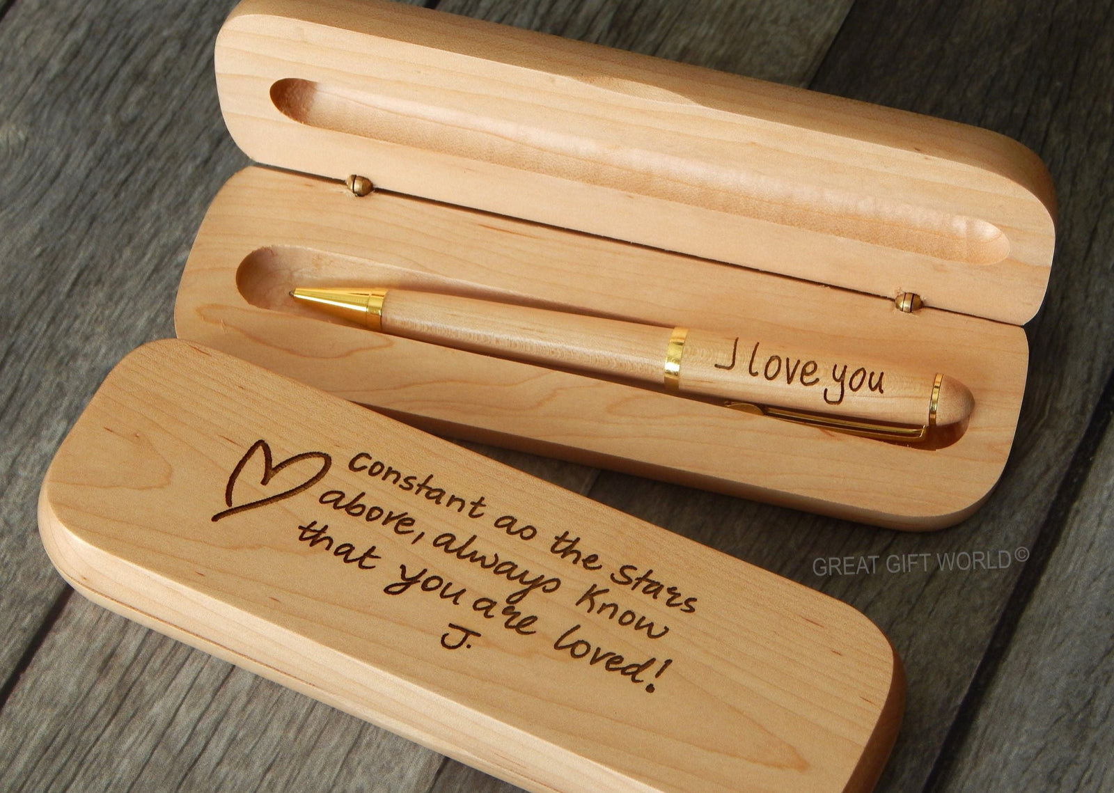 A wooden pen with a gold-tone cap and an engraved message in cursive script, displayed inside a matching wooden case. The pen and case are light-colored, possibly rosewood or maple, and the text reads 'I love you' and 'Constant as the stars above you, I love you.