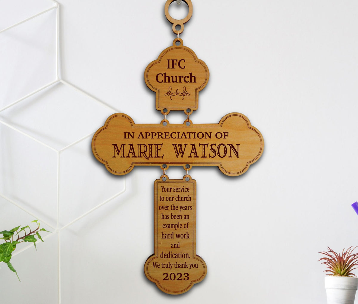 A personalized wooden church appreciation cross plaque hanging on a white wall. The cross is engraved with 'IFC Church' at the top, 'IN APPRECIATION OF MARIE WATSON' in the center, and a message of thanks for hard work and dedication in 2023.
