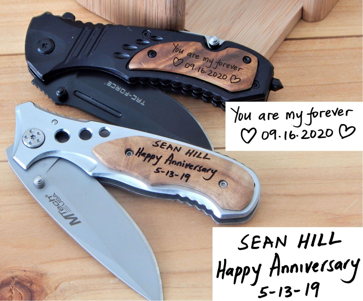 Two personalized folding pocket knives displayed on a wooden surface, one black and one silver, both with engraved wood handles. White text boxes with handwritten anniversary messages are overlaid on the right side.