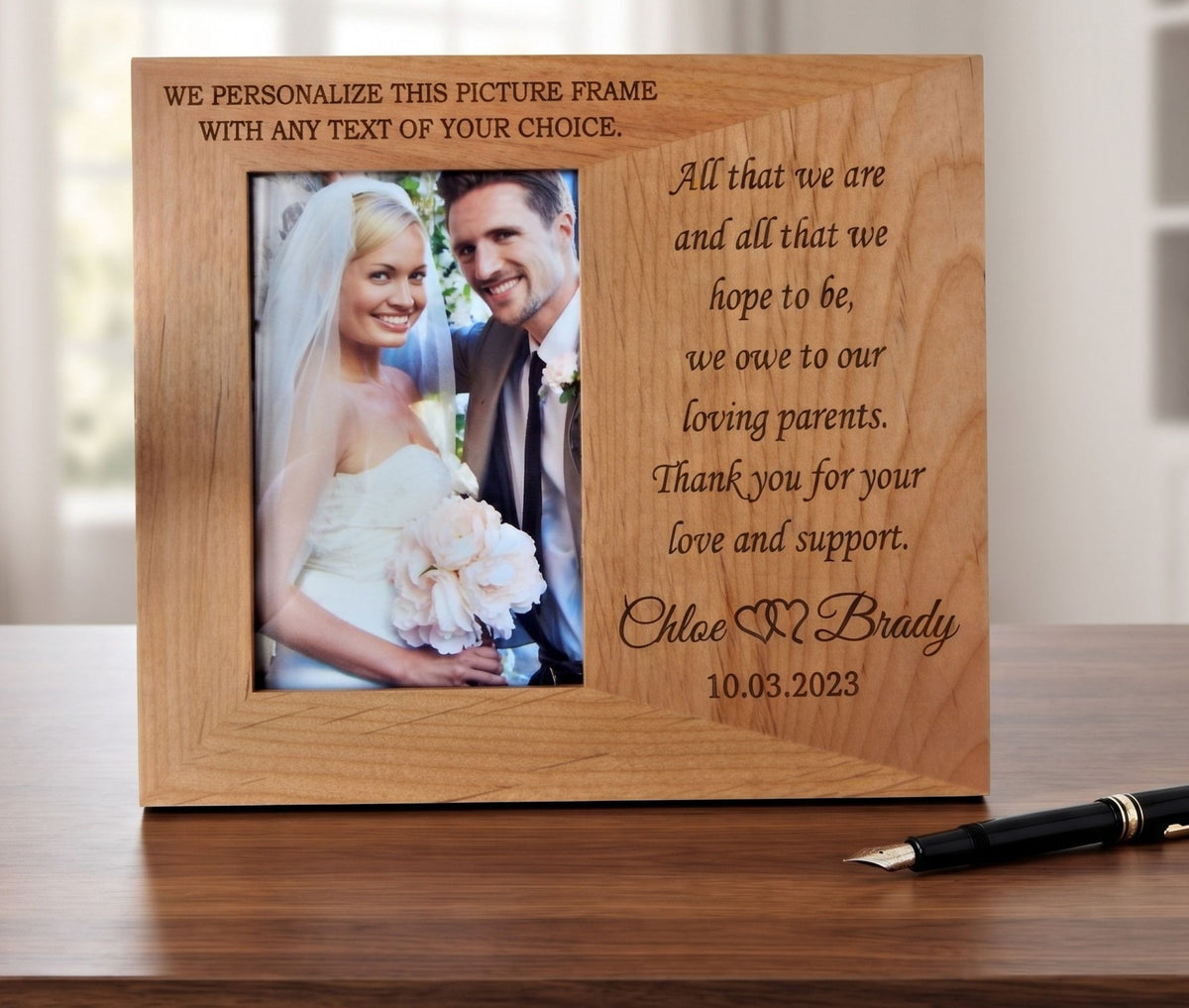 A personalized wooden picture frame with engraved text, shown standing on a wooden table. The frame has a photo of a bride and groom on the left and a message to parents on the right.