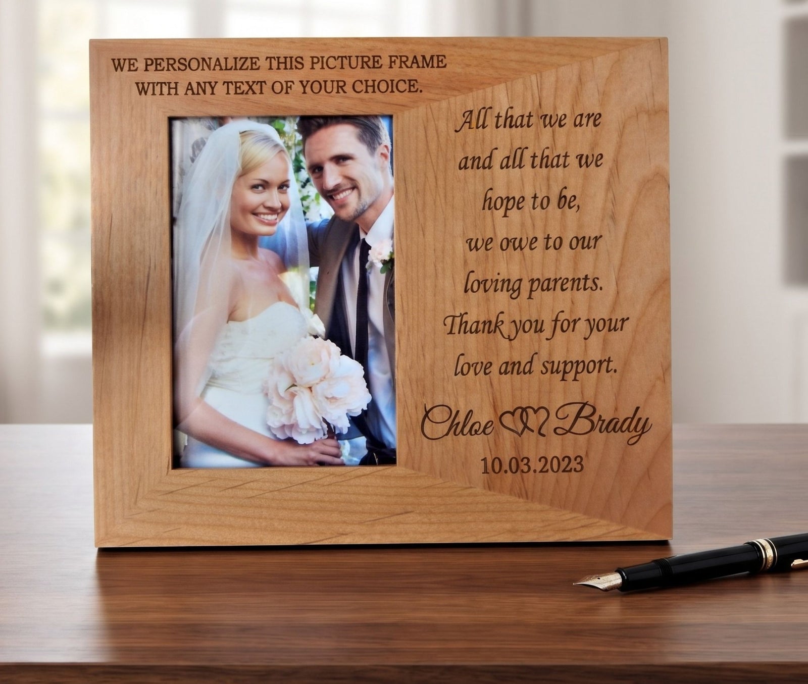 A personalized wooden picture frame with engraved text, shown standing on a wooden table. The frame has a photo of a bride and groom on the left and a message to parents on the right.